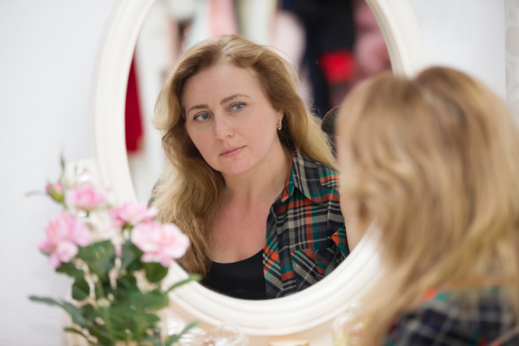 Woman realising menopause is coming - looking in mirror seeing changes to her face & hair